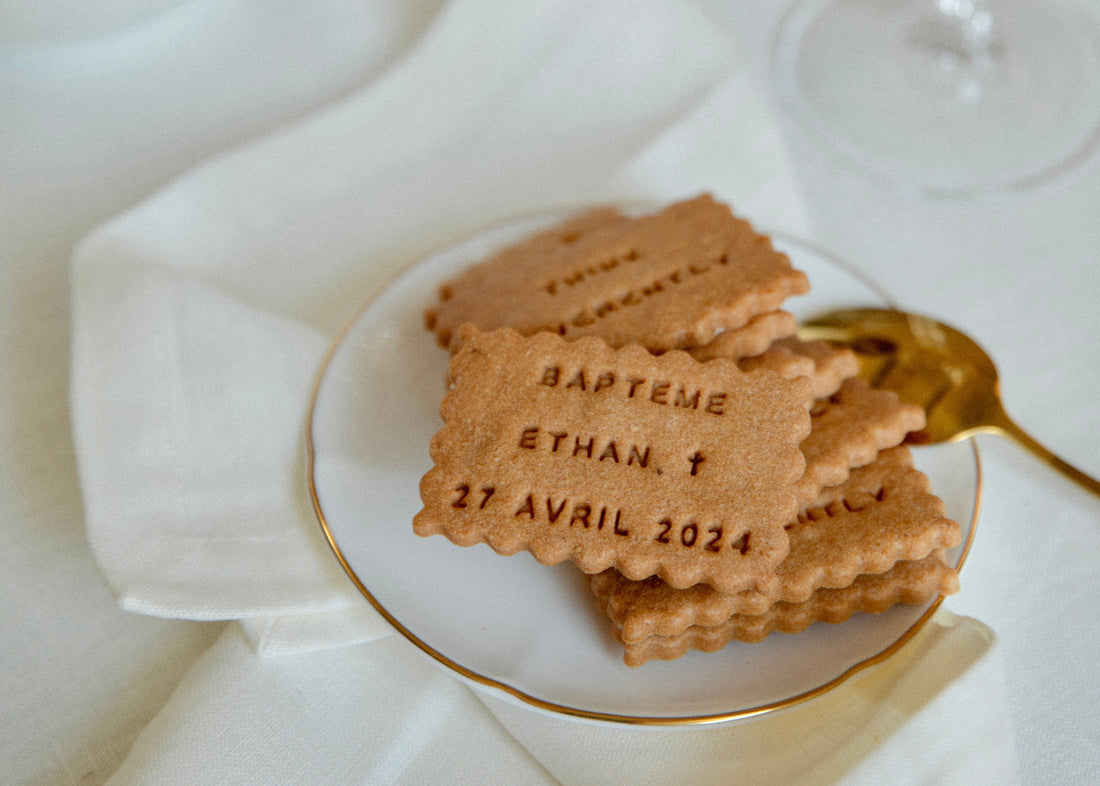 Biscuit personnalisé en forme de petit beurre avec l'inscription "Baptême - Ethan - Avril", posé sur une table de baptême au style élégant.