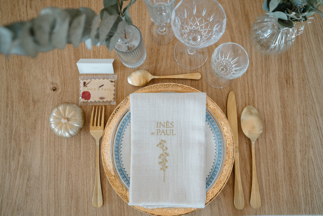 Biscuit avec pétales de fleurs et nom des mariés posé sur une table de mariage dorée